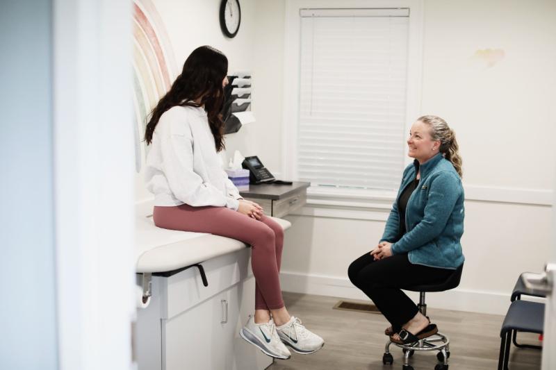 a doctor sitting on a stool talking to a patient on an exam table