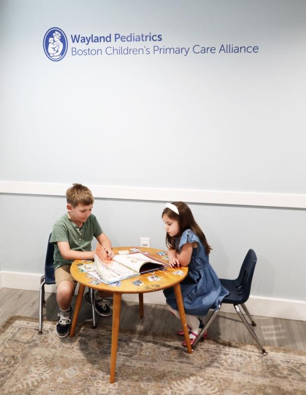 two children sitting at a small table under a sign for wayland pediatrics